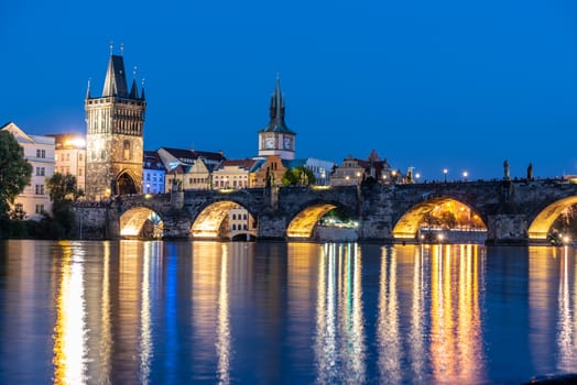 Illuminated Charles Bridge reflected in Vltava River. Evening in Prague, Czech Republic.