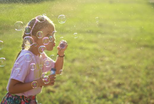 Cute girl blowing soap bubbles, bubbles in focus