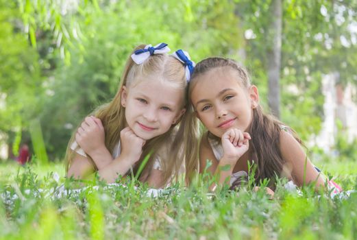 Two smiling girls lying on green  grass in the park in summer
