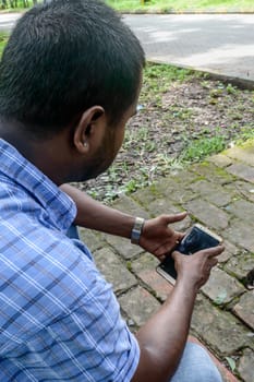 Close up of a mam sitting in a park and using mobile smart phone.