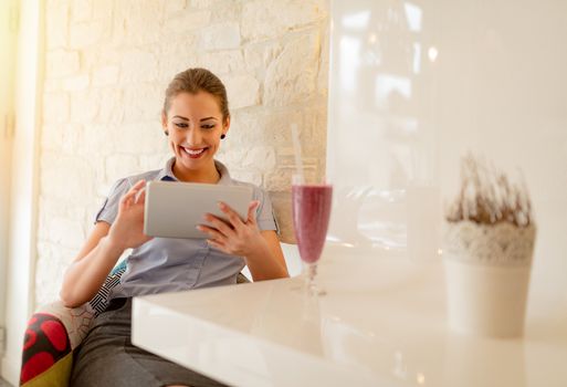 Young smiling businesswoman on a break in a cafe. She is using digital tablet and drink coffee. 