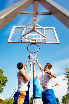 Four basketball players have a training outdoor. They are playing and jumping for alley oop.