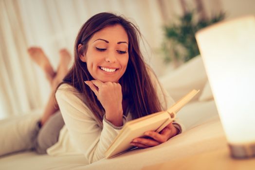 Beautiful smiling girl relaxing in bed and reading book. 