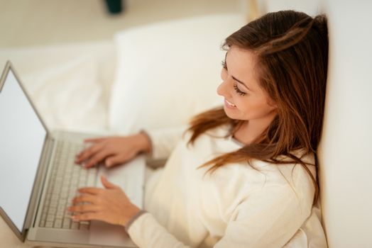 Beautiful smiling girl relaxing in bed and working on laptop. 