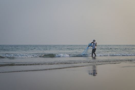 Male fisherman catching fish one evening summer day with fishing net, the traditional way of fishing of a small village in coast of Indian. The Subject of the image is exciting, sensational and calm. This photography is taken in as landscape style may be used as a background, wallpaper, screen saver.