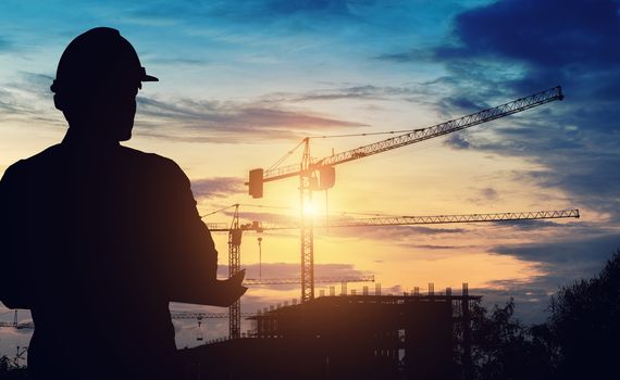 Silhouette engineers are standing survey work on construction over blurred Worker in  construction site and sunset.