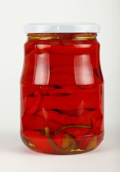 Close up of one glass jar of pickled red hot cherry chili pepperoncini peppers over white background, low angle side view