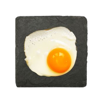 Close up one sunny side fried egg served on black slate board plate isolated on white background, elevated top view, directly above