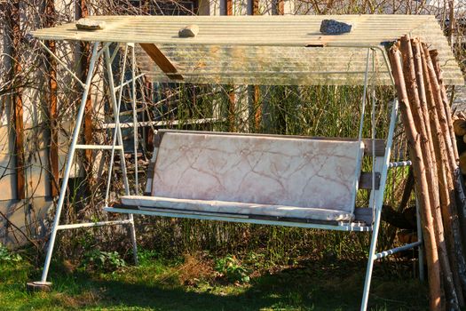 Old homemade porch swing, Hollywood swing on a meadow surrounded by plants in the garden with a fence and trees.