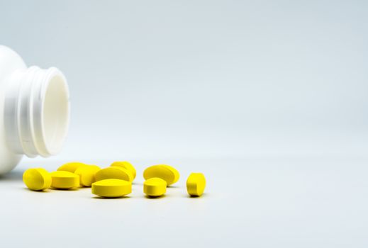 Yellow oval tablet pills and opened white bottle on white background with beautiful creative pattern and copy space for text. Mild to moderate pain management. Pain killer medicine. Pharmaceutical industry. Pharmacy background. Global healthcare concept. NSAIDs drug.