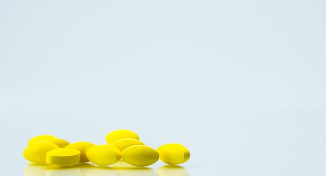 Pile of yellow oval tablet pills on white background with copy space for text. Mild to moderate pain management. Pain killer medicine. NSAIDs drug. Pharmaceutical industry. Pharmacy and pharmacology background. Global healthcare concept.