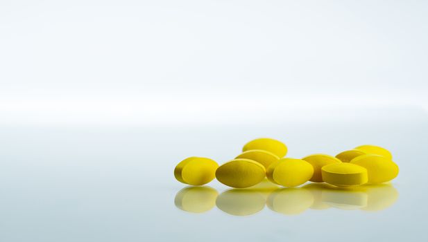 Pile of yellow oval tablet pills on white background with copy space for text. Mild to moderate pain management. Pain killer medicine. Medicine for relieve high fever. NSAIDs drug. Pharmaceutical industry. Pharmacy background. Global healthcare concept.