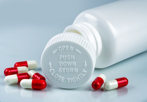 Capsules pills on white background and plastic bottle with blank label and copy space. Childproof packaging. Child resistant pill container. Push down and turn cap.Global healthcare and love concept. Pharmaceutical industry. Pharmacy background.