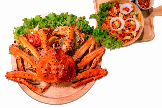 Cooked Alaskan king crab served with vegetable salad isolated on white background. Red Alaskan king crab legs on vintage wooden plate background. Seafood for lunch or luxury dinner.