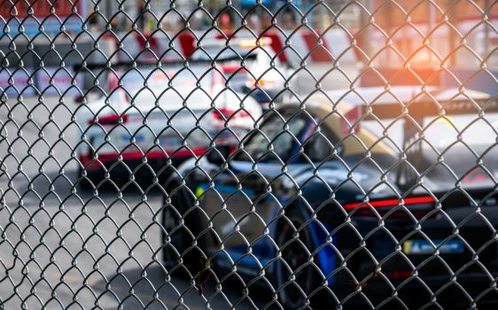 Motorsport car racing on asphalt road. View from the fence mesh netting on blurred car on racetrack background. Super racing car on street circuit. Automotive industry concept.