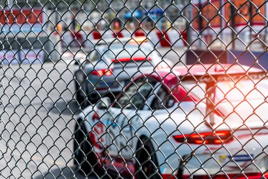 Motorsport car racing on asphalt road. View from the fence mesh netting on blurred car on racetrack background. Super racing car on street circuit. Automotive industry concept.