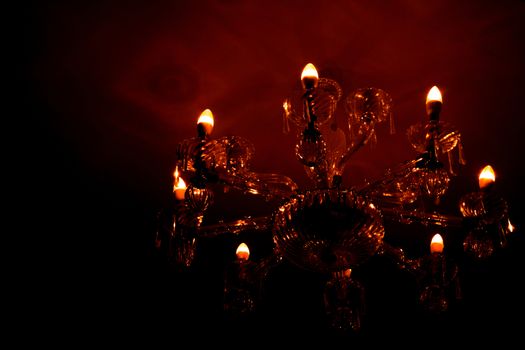 Luxury glass chandelier mounted on ceilings of the room. Red warm light from chandelier reflection on the wall.