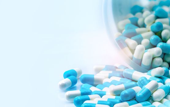 Blue and white capsules pill spilled out from white plastic bottle container. Global healthcare concept. Antibiotics drug resistance. Antimicrobial capsule pills. Pharmaceutical industry.