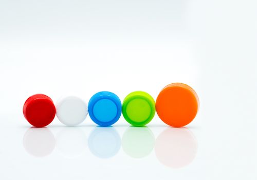 Different size of white, green, red, blue and orange color round plastic screw caps in a line on white background and copy space.