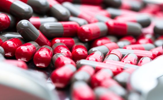 Macro shot detail of red and grey capsule pills on stainless steel drug tray. Pharmaceutical industry. Pharmacy background. Global healthcare concept. Health budgets and policy.
