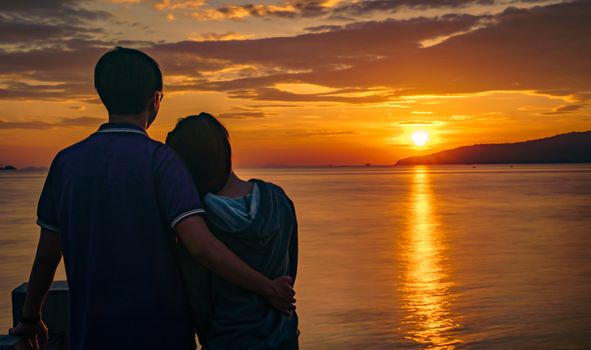 Silhouette of attractive young romantic couple in love is hugging on the beach at sunrise with beautiful golden sky. Vacation and travel concept. Romantic young couple dating at seaside.