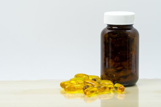 Yellow fish oil capsule pills with amber glass bottle with blank label on the table with copy space for text. Vitamins and supplements for heart care and joint care. Source of omega 3, EPA and DHA. Pharmaceutical industry. Global healthcare concept.