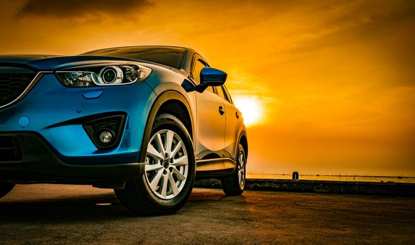 Blue compact SUV car with sport and modern design parked on concrete road by the sea at sunset. Environmentally friendly technology. Business success concept. Automotive industry. Hybrid car and road trip concept.