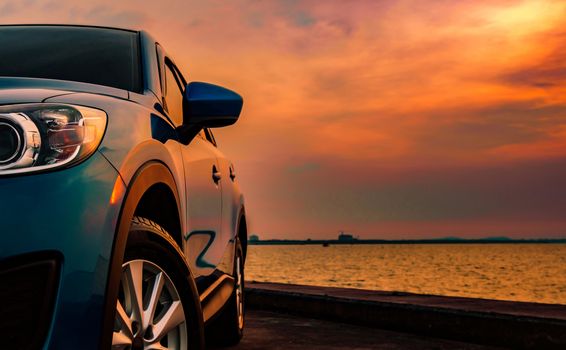 Blue compact SUV car with sport and modern design parked on concrete road by the sea at sunset. Environmentally friendly technology. Business success concept. Automotive industry. Hybrid car and road trip concept.