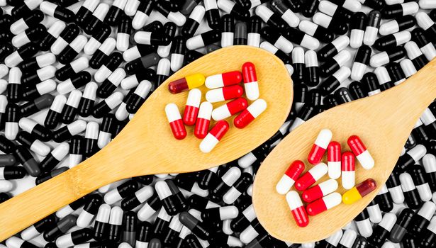 Colorful of antibiotics capsule pills in wooden spoon on black and white background of capsules. Drug resistance concept. Antibiotics drug use with reasonable and global healthcare concept. Pharmaceutical industry. Pharmacy background.