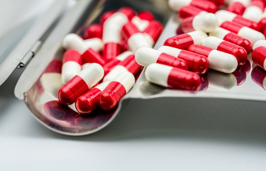 Red, white antibiotic capsules pills on stainless steel drug tray. Drug resistance, antibiotic drug use with reasonable, health policy and health insurance concept. Pharmaceutical industry. Pharmacy background.