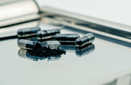 Selective focus on powders of activated charcoal on stainless steel drug tray and blur capsule background. Black powders medicine in capsule. Pharmaceutical products. Pharmacy background.