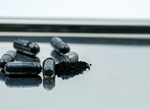 Selective focus on powders of activated charcoal on stainless steel drug tray and blur capsule background. Black powders medicine in capsule. Pharmaceutical products. Pharmacy background.