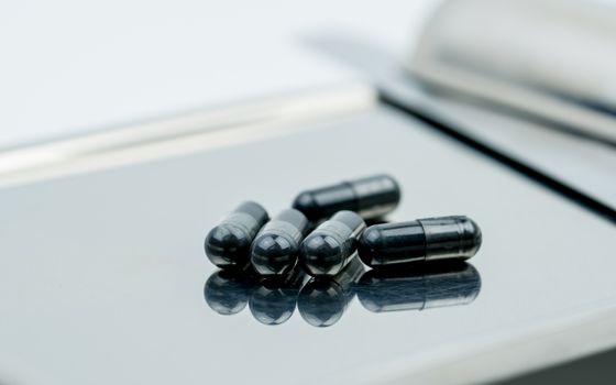 Selective focus on powders of activated charcoal on stainless steel drug tray and blur capsule background