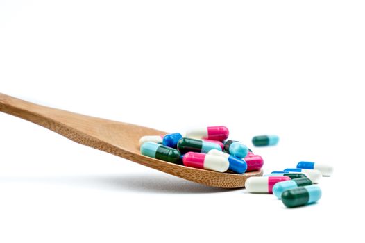 Colorful of antibiotics capsule pills in wooden spoon are spilling on white background with copy space. Antibiotic drug use with reasonable. Pharmaceutical industry. Pharmacy background. Health budgets and policy. Antimicrobial drug overuse.