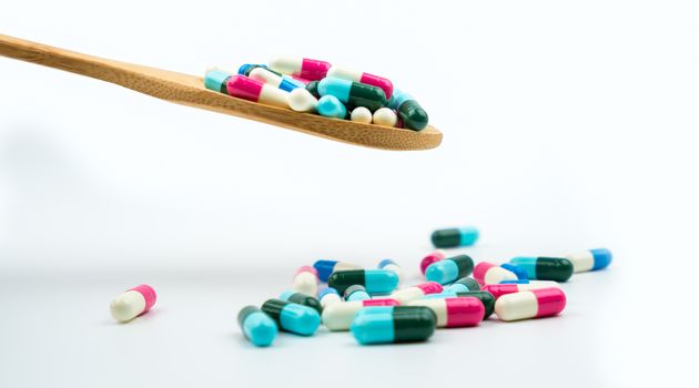 Colorful of antibiotics capsule pills in wooden spoon are spilling on white background with copy space. Antibiotic drug use with reasonable. Pharmaceutical industry. Pharmacy background. Health budgets and policy. Antimicrobial drug overuse.