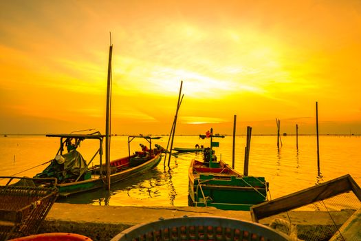 Fisherman's boat floating in the sea near bamboo pole at sunset in Thailand.