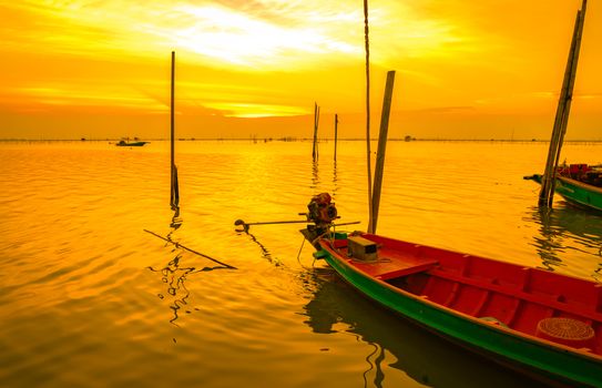 Fisherman's boat floating in the sea near bamboo pole at sunset in Thailand.