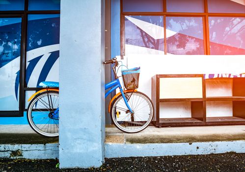 Bicycle leaning on a pole near a wooden shoe rack placed on a cement floor in a building with flare light. Vintage style.