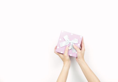 Closeup beautiful and healthy woman hands with neat manicure are holding pink gift box with polka dotted pattern isolated on white background