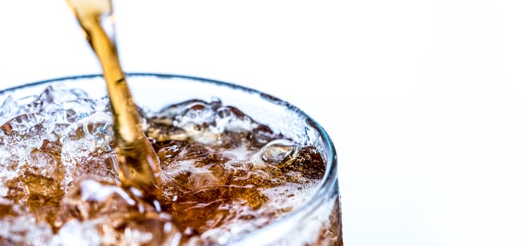 Closeup of soft drink pouring to glass with ice isolated on white background with copy space.