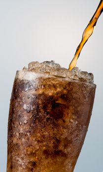 Closeup of soft drink pouring to glass with crushed ice cubes isolated on white background with copy space. There is a drop of water on the transparent glass surface.