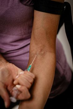 Close-up of a female drug addiction with a belt around her arm injecting drugs with syringe.