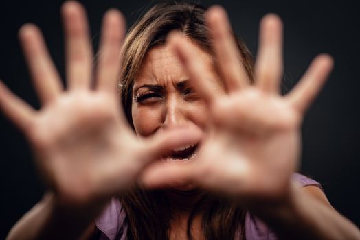 Young abused woman defending with pray looking at camera with outstretched arm. Selective focus. Focus on background, on woman face.