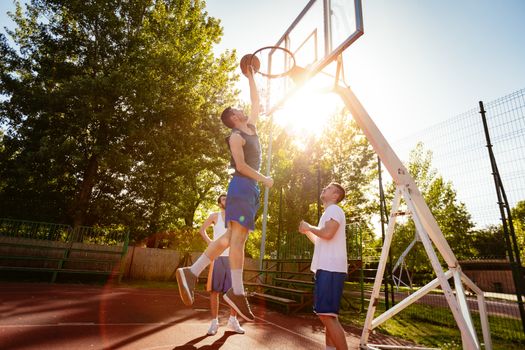 Young basketball players have a training on street court. They are playing and making action together. Young man throw ball to hoop. 