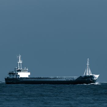 Blue bulk carrier moving from the sea in cold winter. Monochrome