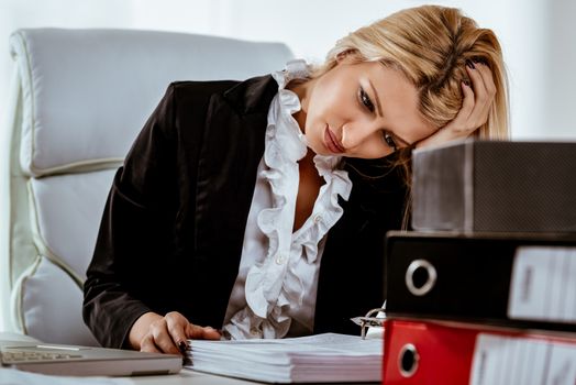 Young tired businesswoman worried sitting in the office. In front of her is a bunch of binders.