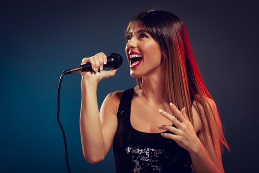 A young smiling woman singer holding a microphone and sing.