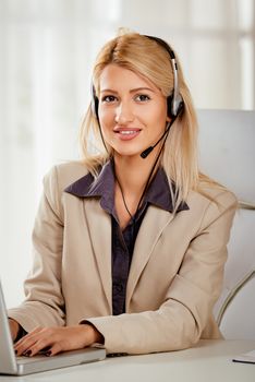 Beautiful smiling woman sitting at the office with a headset on her head and looking at the camera.