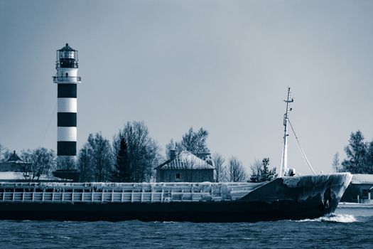 Blue bulk carrier moving from the sea in cold winter. Monochrome