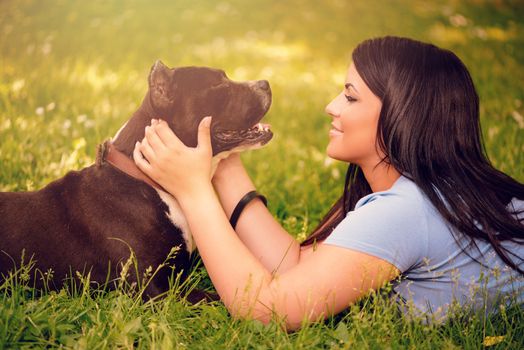 Beautiful young woman with her cute stafford terrier lying on grass in the park.